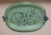 Blue-green platter with black outline of two rabbits sitting close.