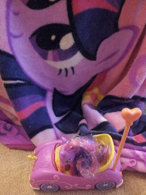 Next to a blanket with a Twilight Sparkle design is a toy car with that pony in it